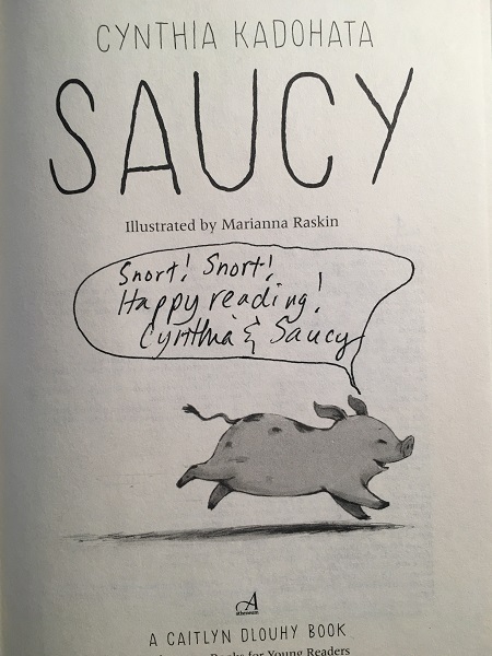 The title page of Saucy, signed by the author Cynthia Kadohata, with the message, written as a speech bubble from Saucy the pig's mouth, "Snort! Snort! Happy reading!"