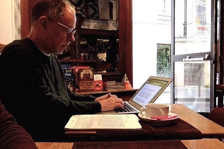 Gregory Maguire writing at a table in a cafe in Paris.