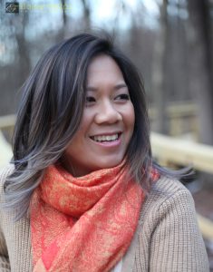 Andrea Wang looking to the side and smiling, wearing a beige sweater and orange paisley scarf.