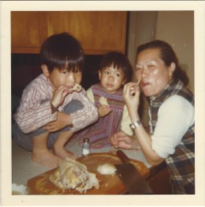 Andrea Wang as a child, eating food with another child and an adult.