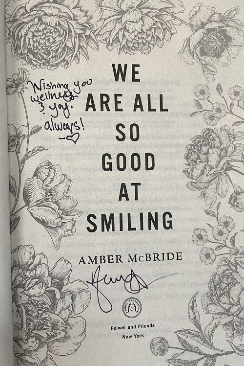 The title page of We Are All So Good at Smiling, signed by the author, Amber McBride, with the message, "Wishing you wellness and joy, always!"