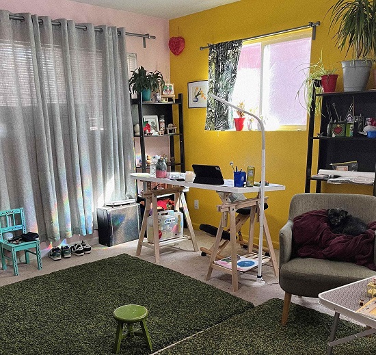 An image of Sendy Santamaria's workspace with her desk next to a bright yellow wall and several small chairs for her son.