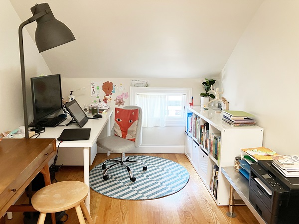 Ann Kim Ha's bright colorful studio, showing a white writing table, and a chair with a pillow designed with a fox face.