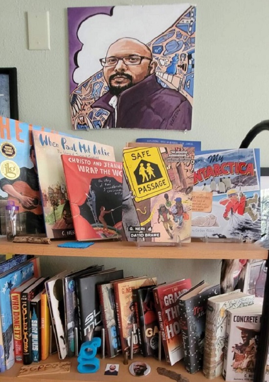 A bookshelf in G. Ner's office featuring his books, below a cartoon portrait of the author.