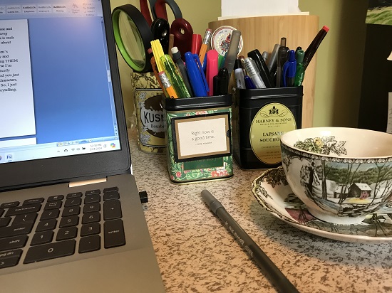 Sally Denmead's computer next to a tea cup and pens in former tea tins.