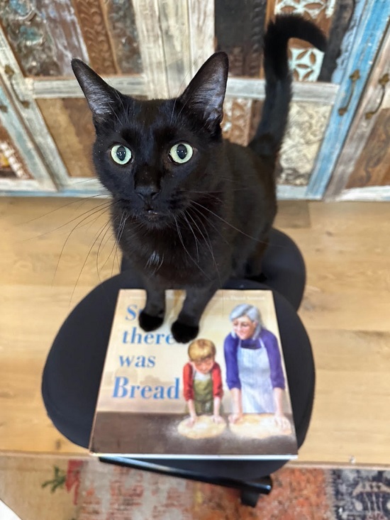 Author Lisl Detlefsen's black cat standing on a copy of Still There Was Bread.