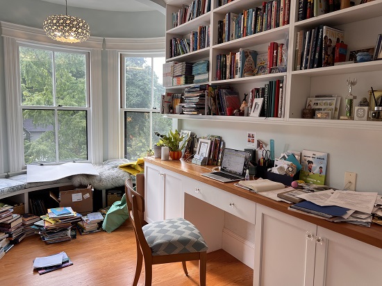 Mia Wenjen's office, showing her desk, bookshelves filled with books, and a rounded wall of windows with a padded bench.