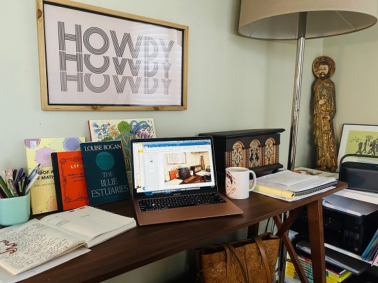 Amy Alznauer's desk featuring art, a cup of coffee, books, a laptop, and journals.